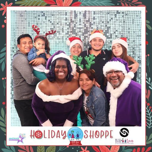Group posing in Santa hats at a holiday shop photo booth, smiling in front of a festive backdrop.
