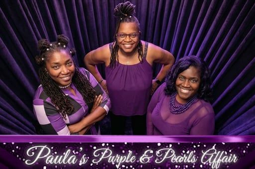 Three women in purple outfits posing against a purple backdrop with “Paula’s Purple & Pearls Affair” text