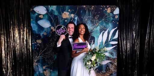 Couple posing with a “Future Mrs.” sign at a floral-themed photo backdrop