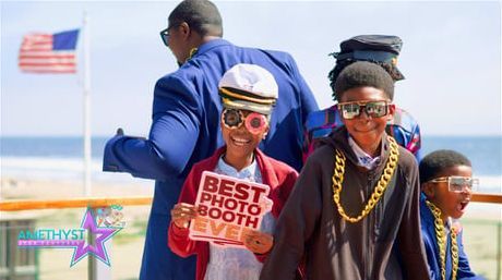 Smiling children in sunglasses and hats at a beach parade, with an American flag and a man in blue nearby