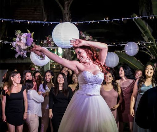 Woman in white dancing with a bouquet under lanterns at an outdoor wedding