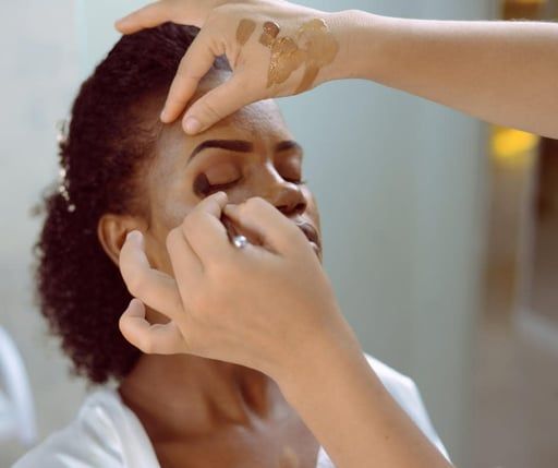 Makeup artist applying eye makeup to a seated person’s face in a bright room