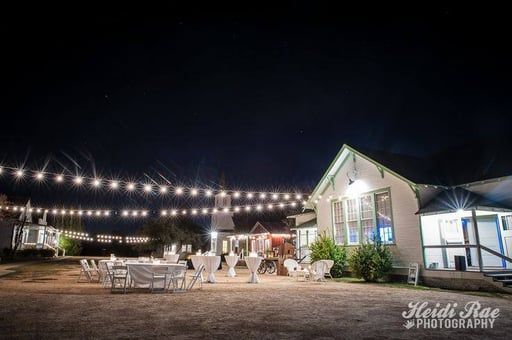 String-lit outdoor patio beside a white event hall at night, with tables and chairs arranged outside.