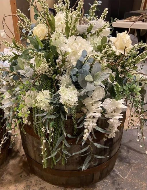 White floral arrangement with greenery in a wooden barrel centerpiece