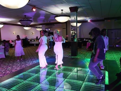 People dancing on a glowing LED floor in a dim banquet hall with purple lighting.