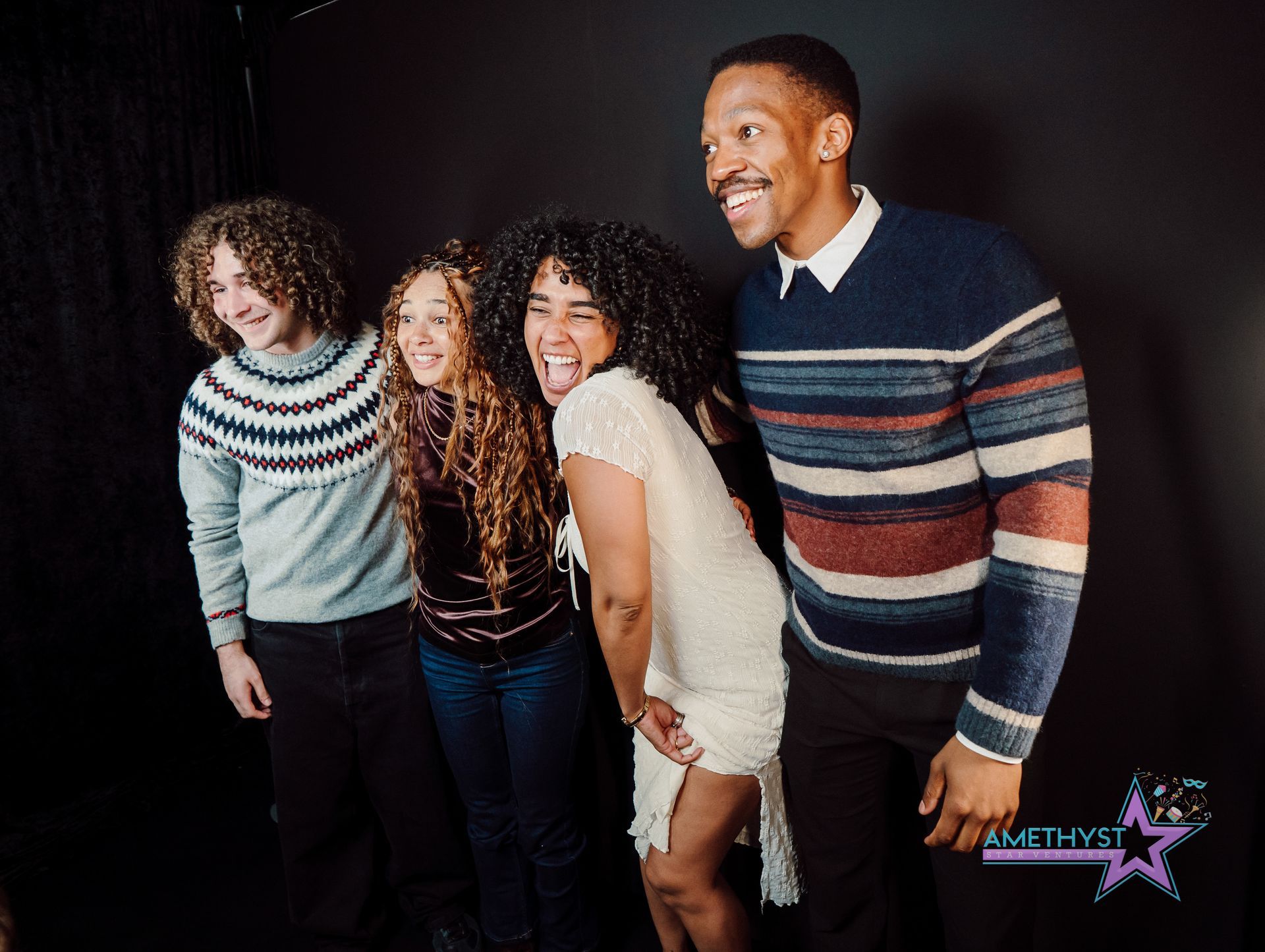 Four smiling people pose together against a dark studio backdrop.