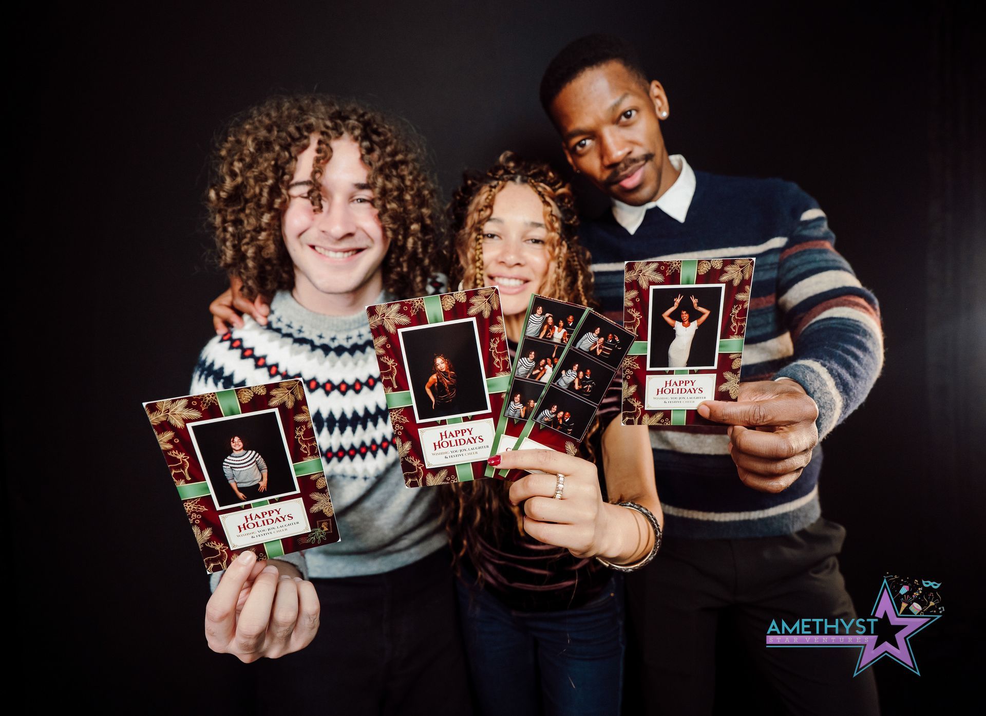 Three people smiling and holding framed holiday cards against a black background.