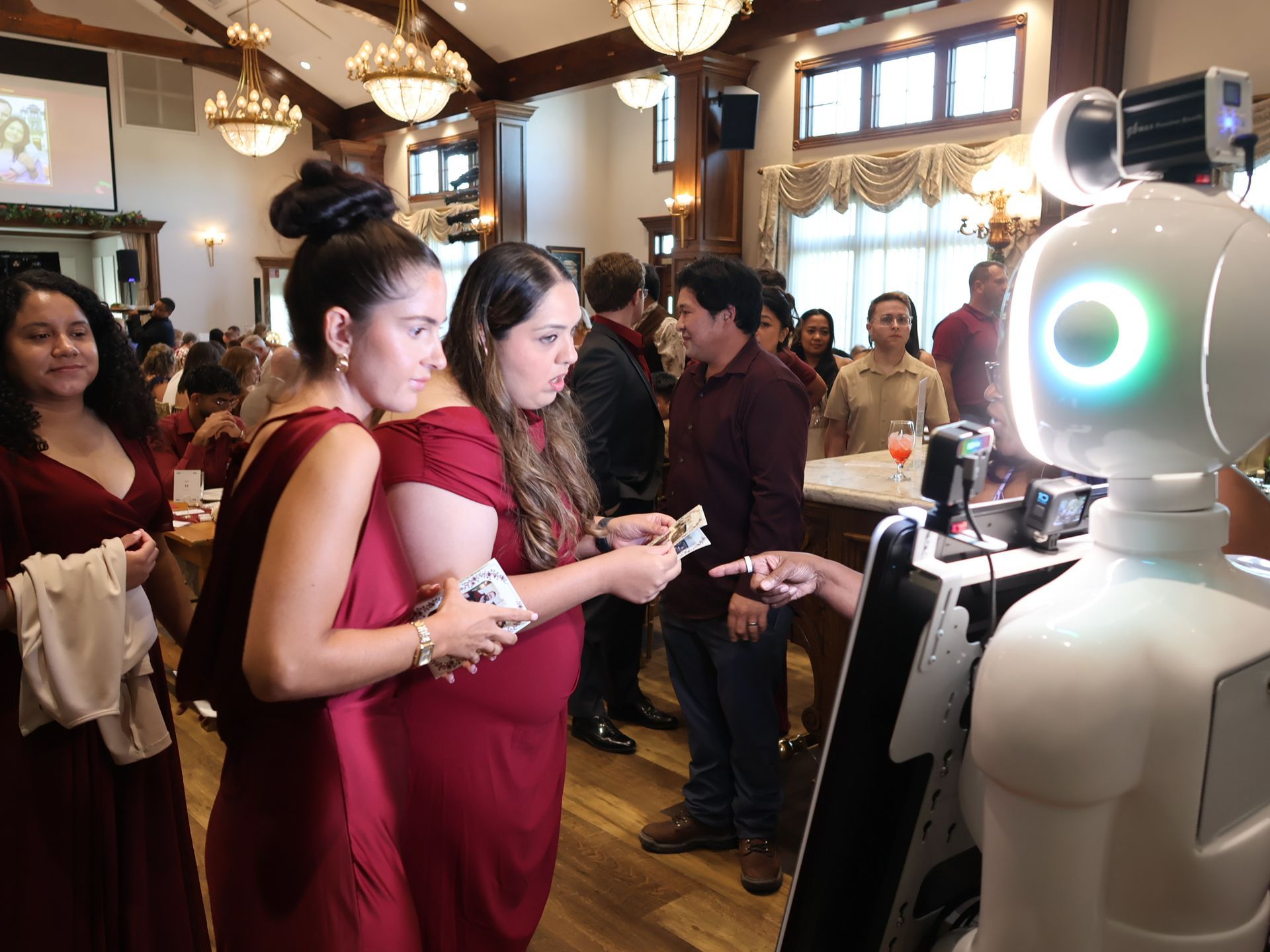 Wedding guests holding custom photo keepsakes beside Starla, a white roaming photo robot, inside Altstadt Brewery