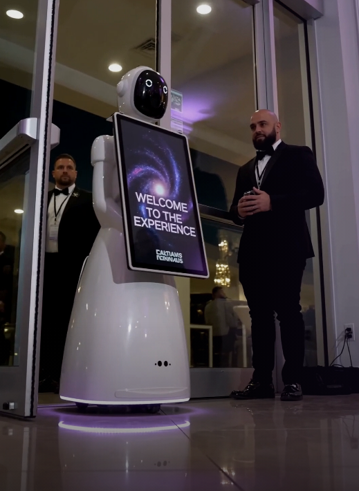 White service robot with “Welcome to the Experience Center” sign at a glass entrance, with two men nearby