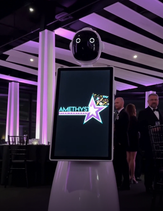Purple-lit robot kiosk with a screen showing the AMETHYS logo and star in an event hall
