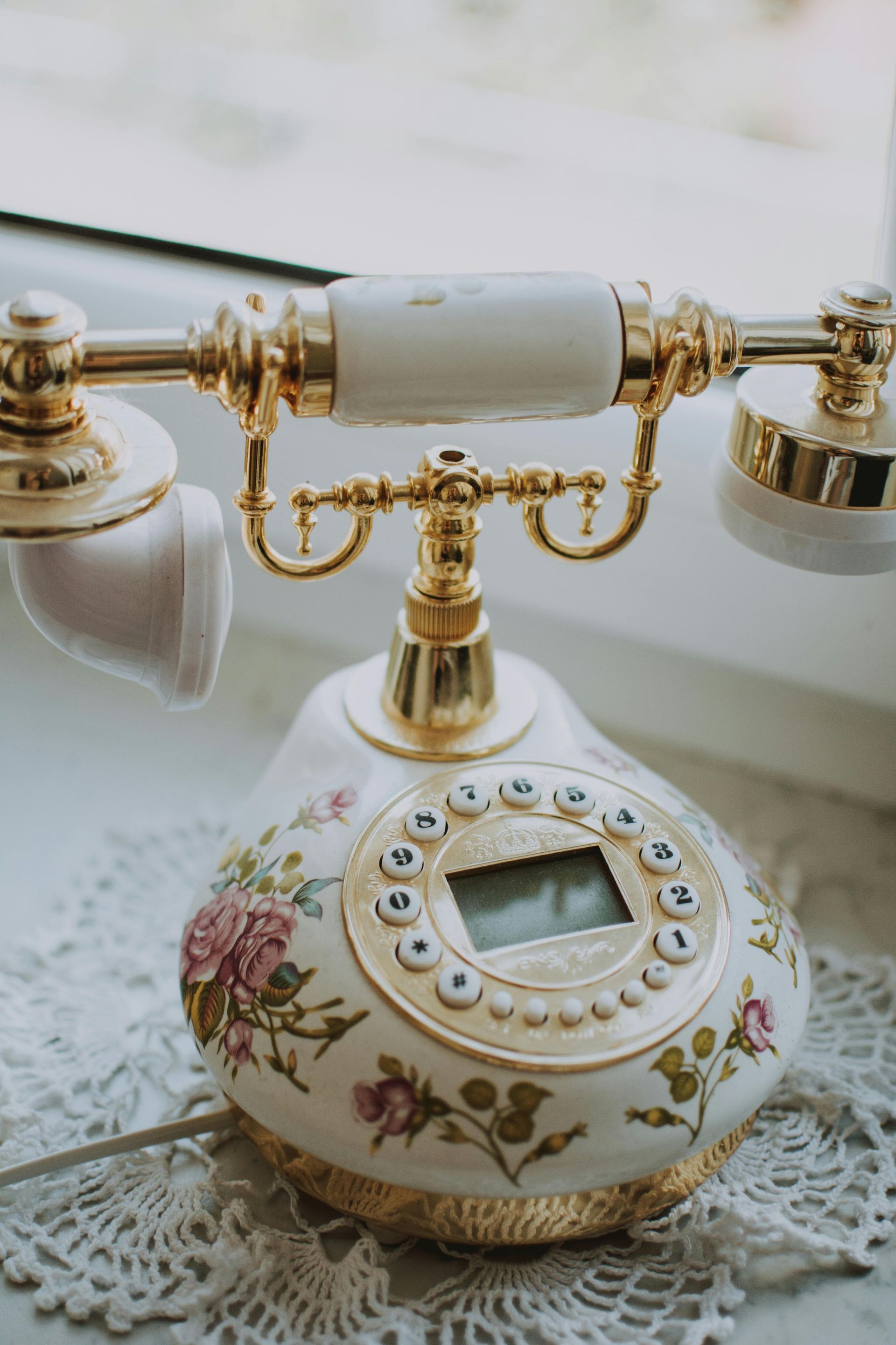 Vintage floral rotary telephone with gold accents on a lace-covered table.