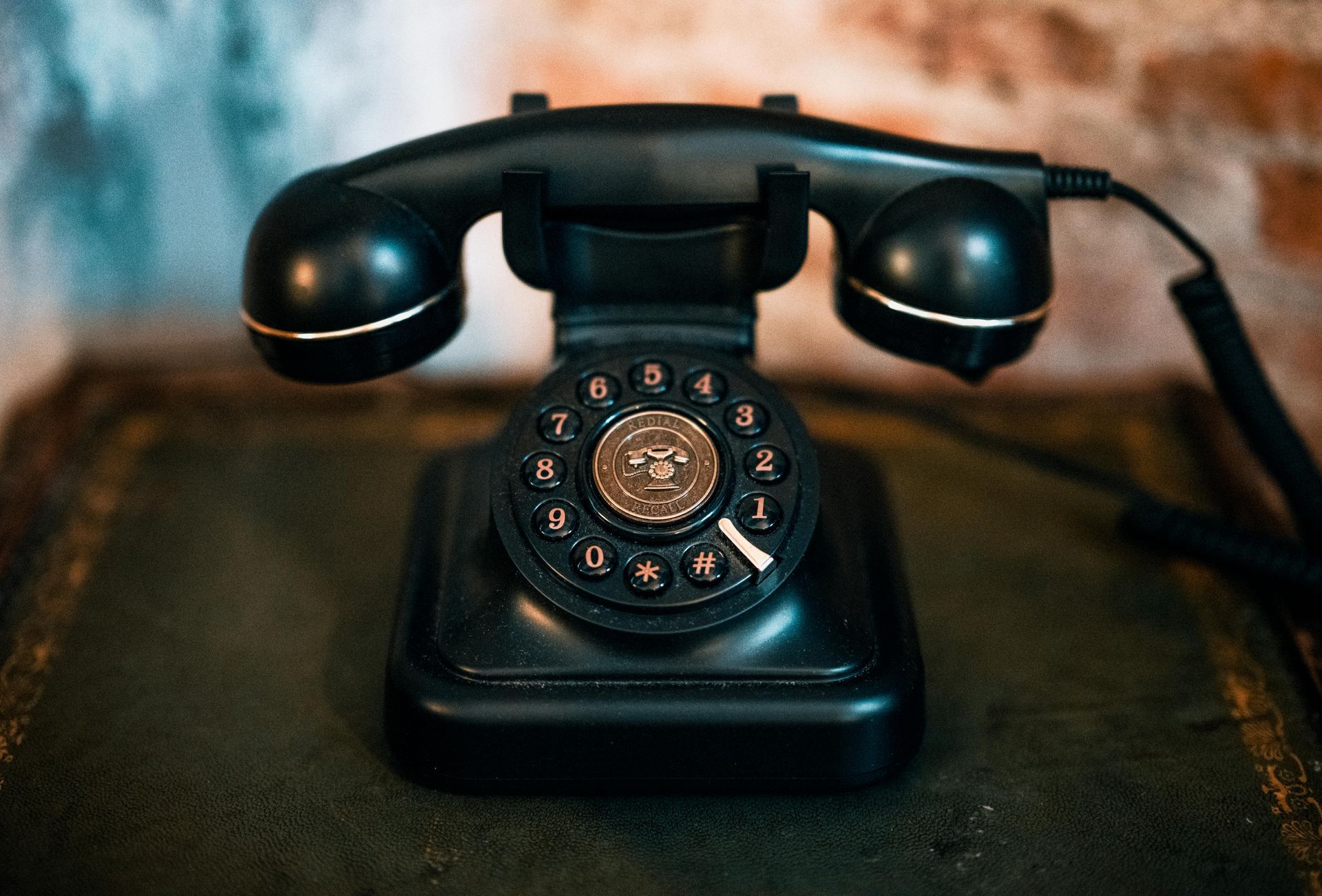 Black rotary dial telephone on a table with a dark cord, against a blurred background.