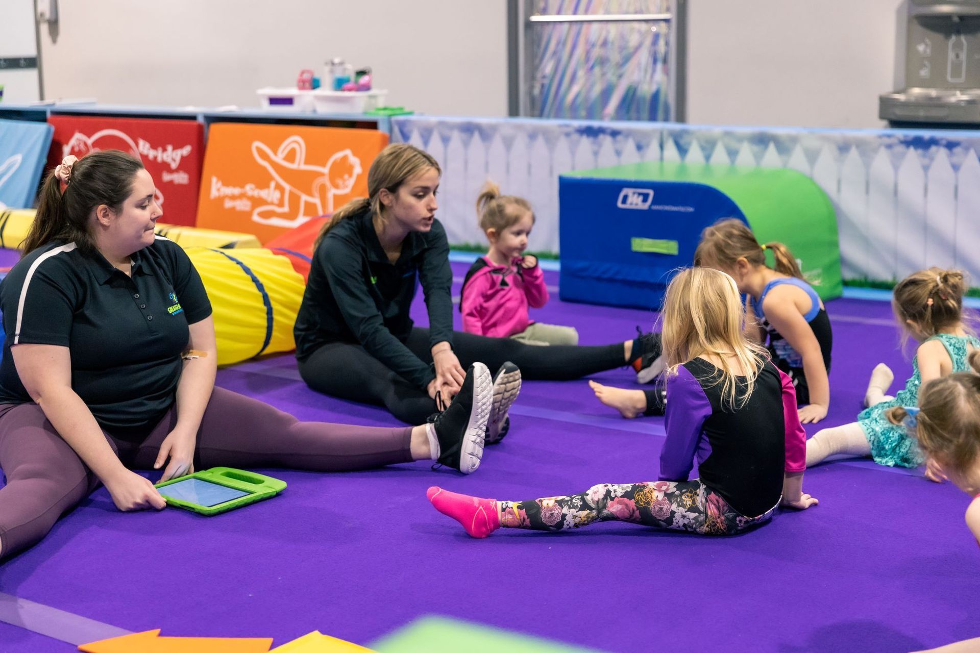 A group of children are sitting on the floor in a gym.