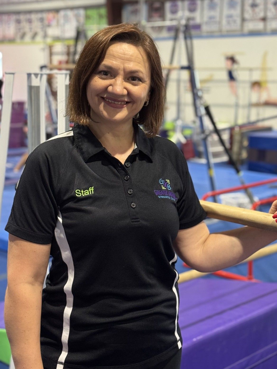 A woman is standing in a gym next to a trampoline.