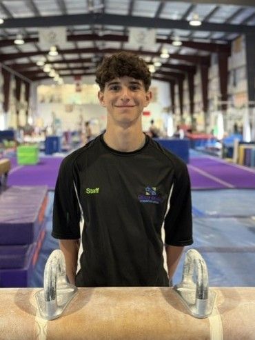 A young man is standing next to a balance beam in a gym.