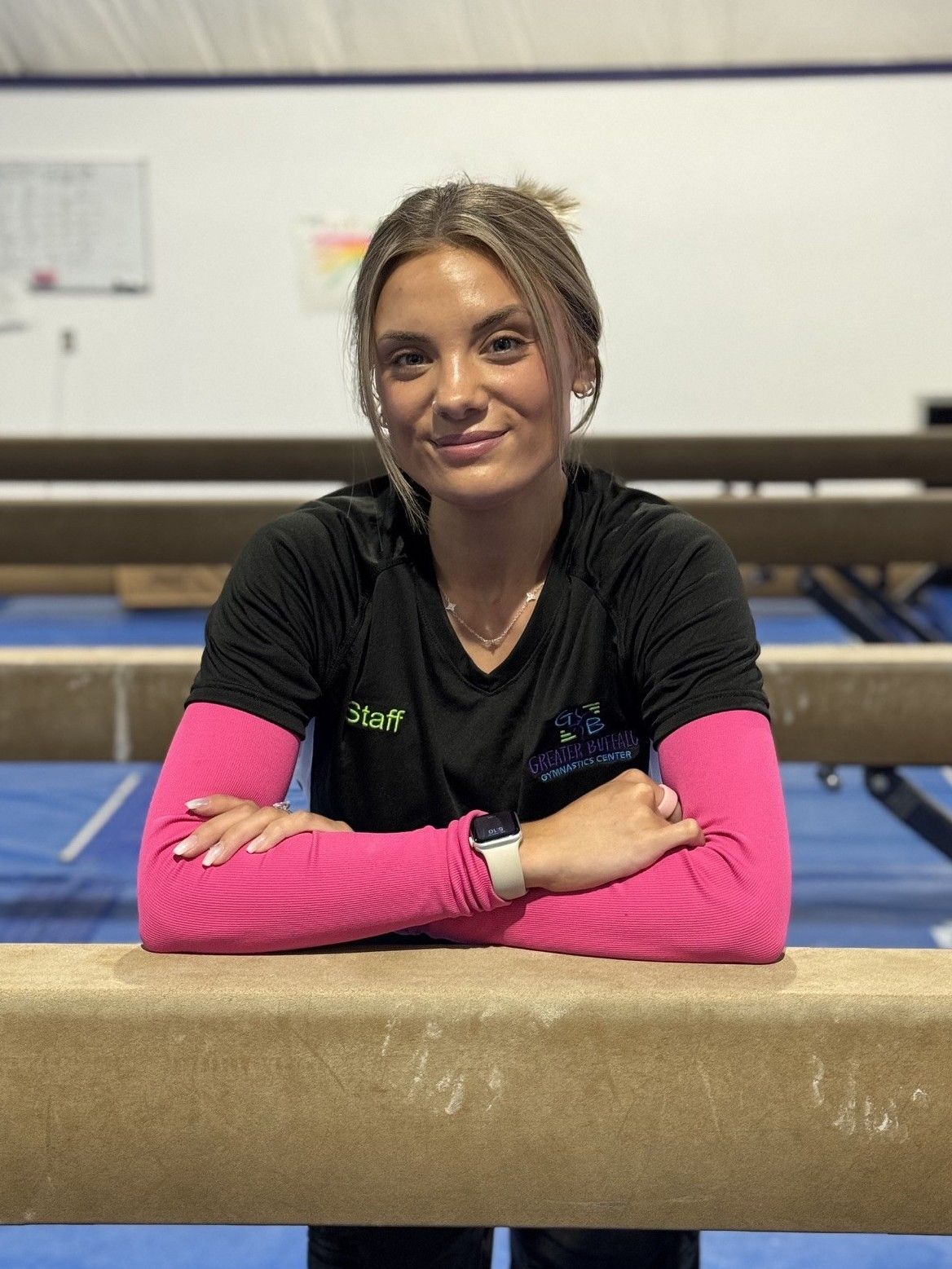 A woman is helping a young girl balance on a balance beam in a gym.
