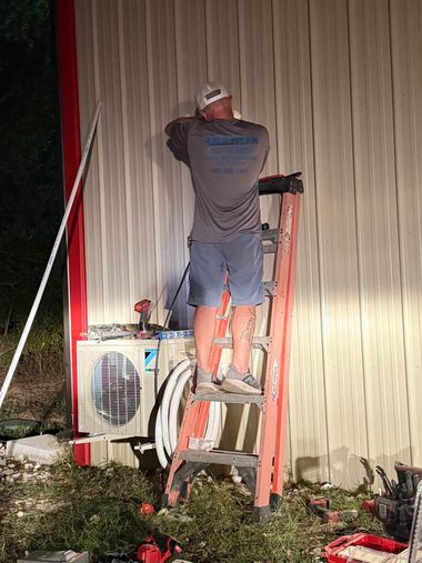 Person on a ladder working on a wall-mounted unit at night outdoors