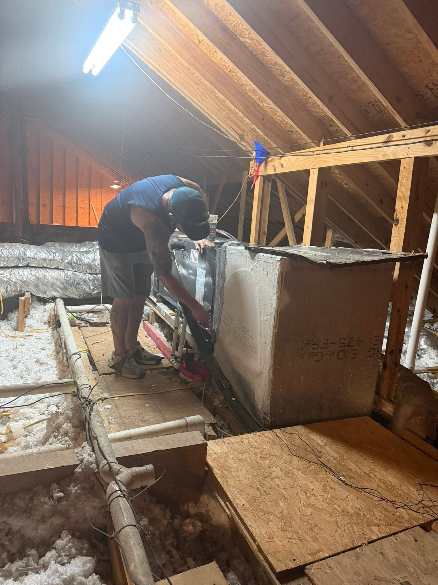 Person working inside an attic, insulating a wall beside exposed wooden beams and floorboards.