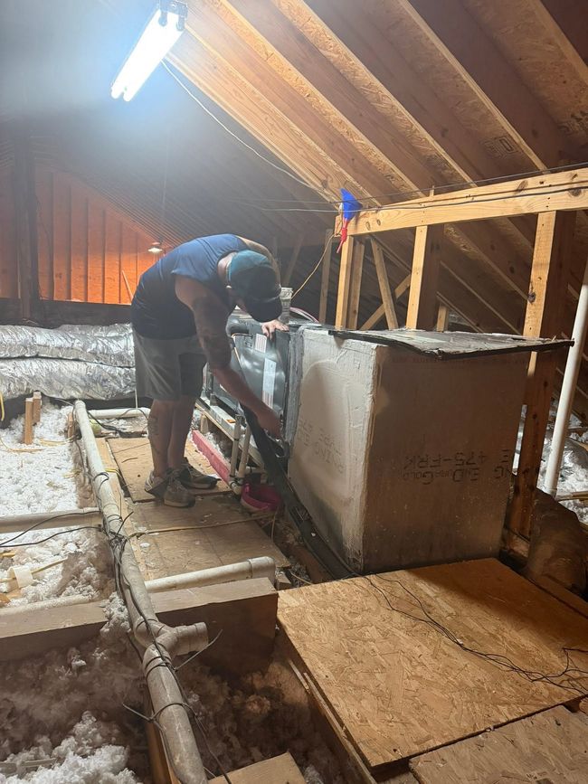 Person working inside an attic, insulating a wall beside exposed wooden beams and floorboards.