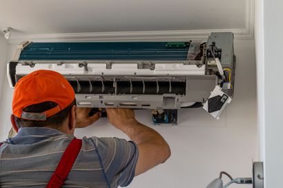 Technician repairing a wall-mounted air conditioner with the cover open