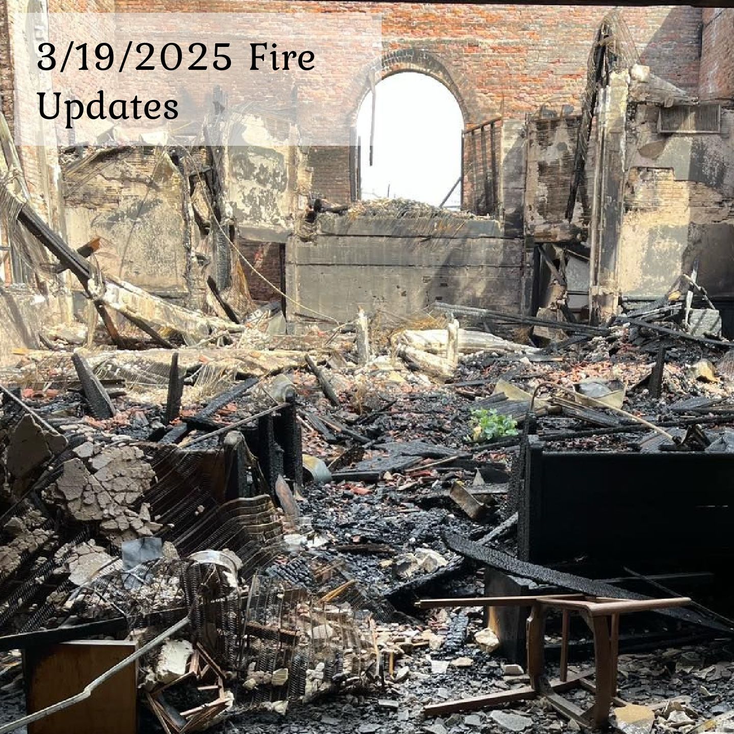 Interior view of a building destroyed by fire, featuring charred debris, exposed brick walls, and a large arched window.