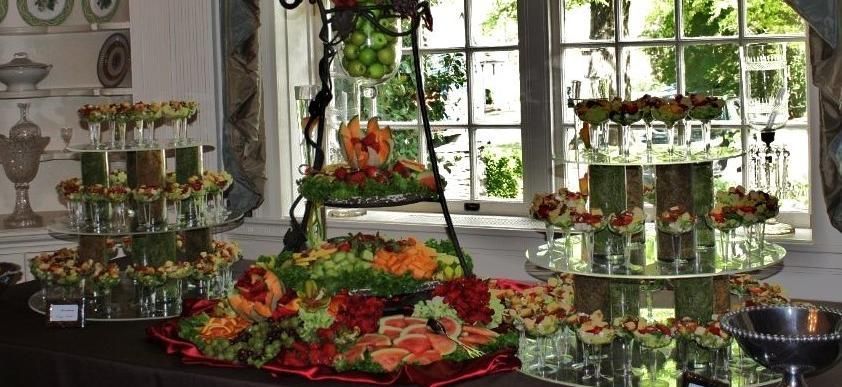 Buffet table with flowers, fruit, and tiered trays in a bright room by a window