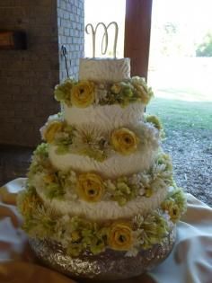 Four-tier white wedding cake with yellow flowers and a silver base, indoors near a doorway