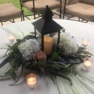 Candlelit floral centerpiece with black lantern and white flowers on a table outdoors