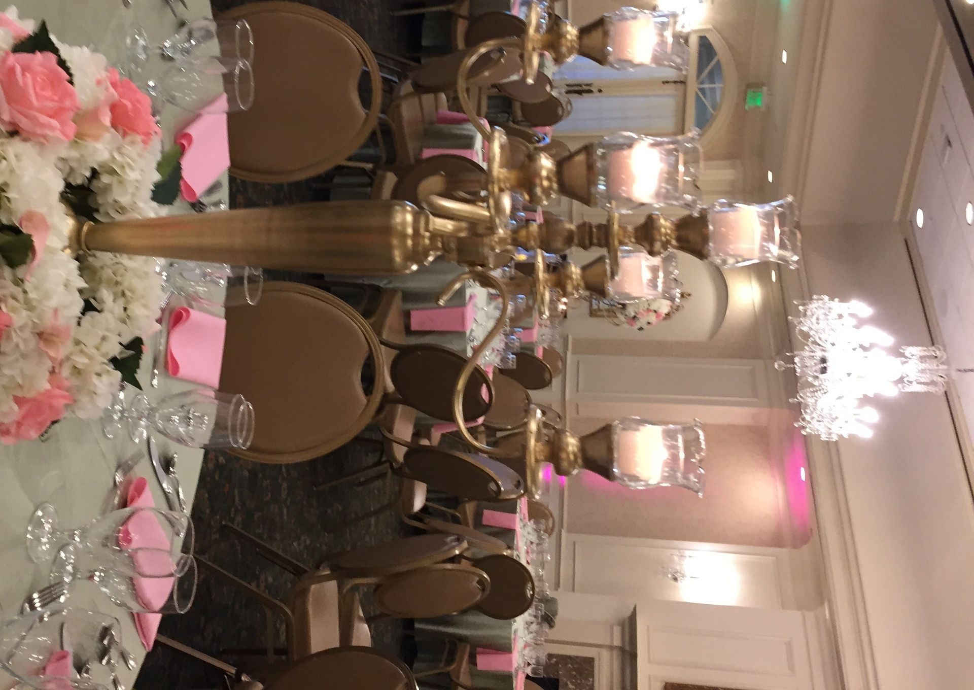Elegant banquet hall with gold chairs, floral centerpieces, chandeliers, and pink uplighting on round tables.