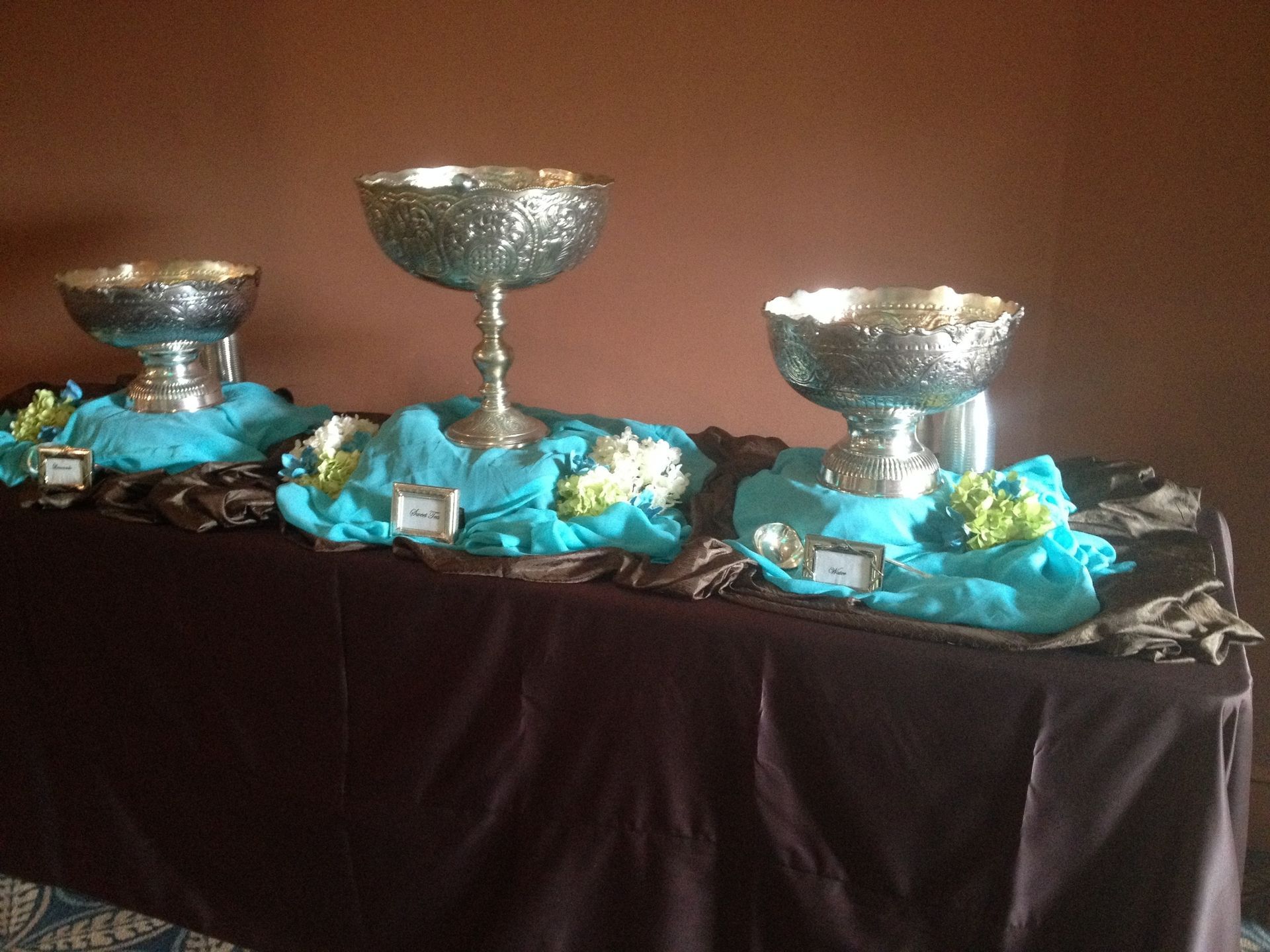 Three silver serving bowls on a table draped with black cloth and blue fabric accents