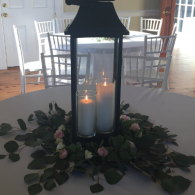 Candle lantern centerpiece with white candles and greenery on a round table in a dining room
