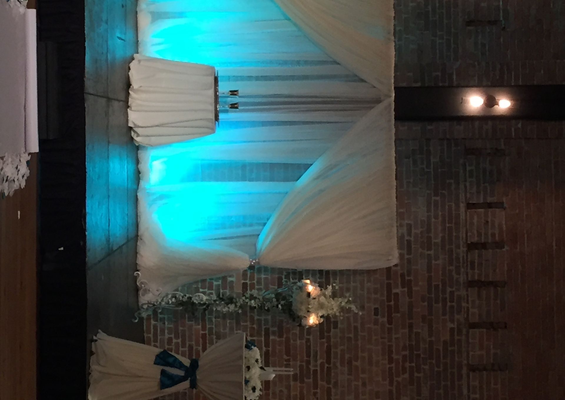 White draped stage with teal uplighting and floral decor in a brick-walled venue