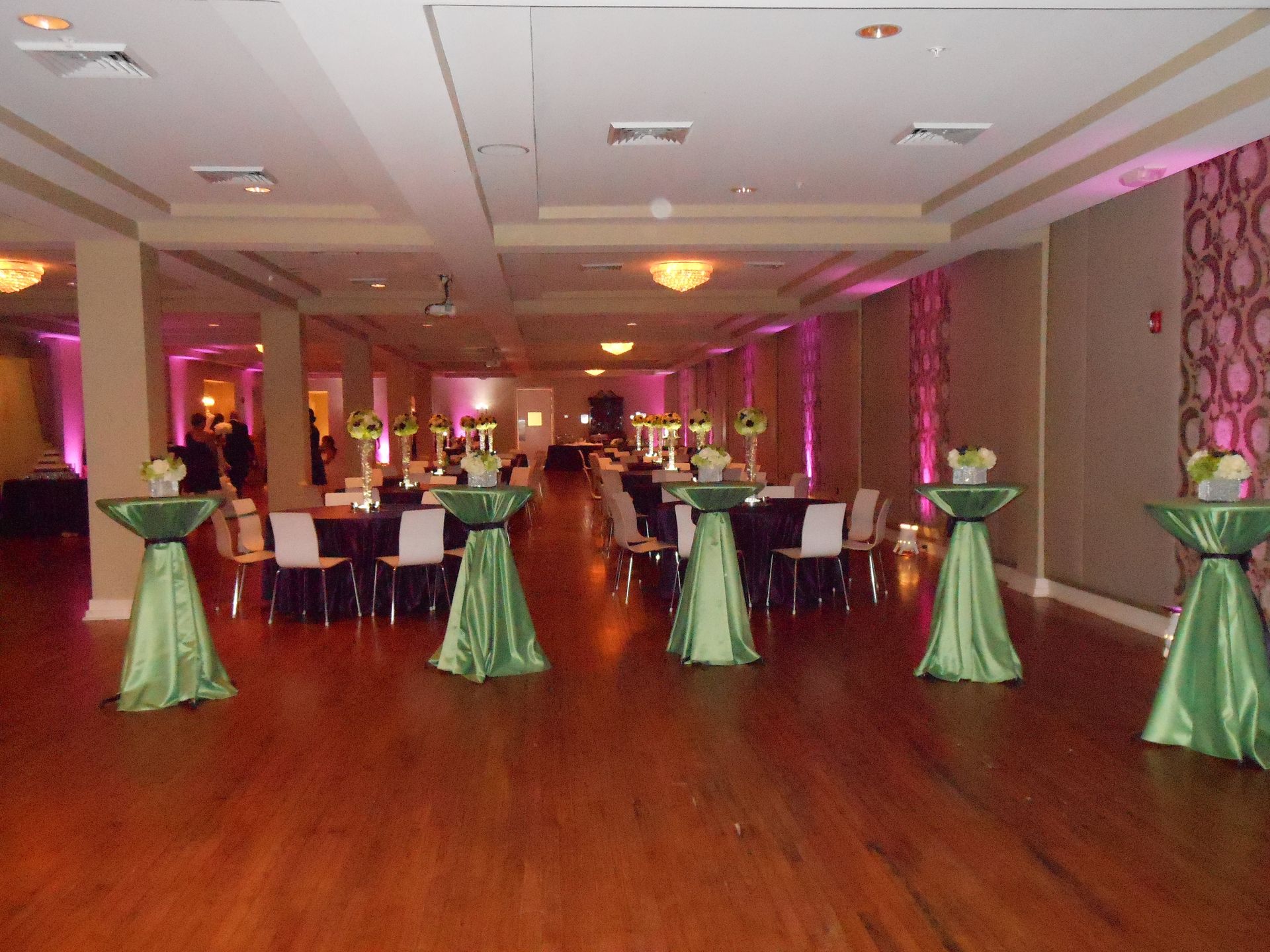 Elegant banquet hall with round tables, green cocktail tables, and pink uplighting on the walls.