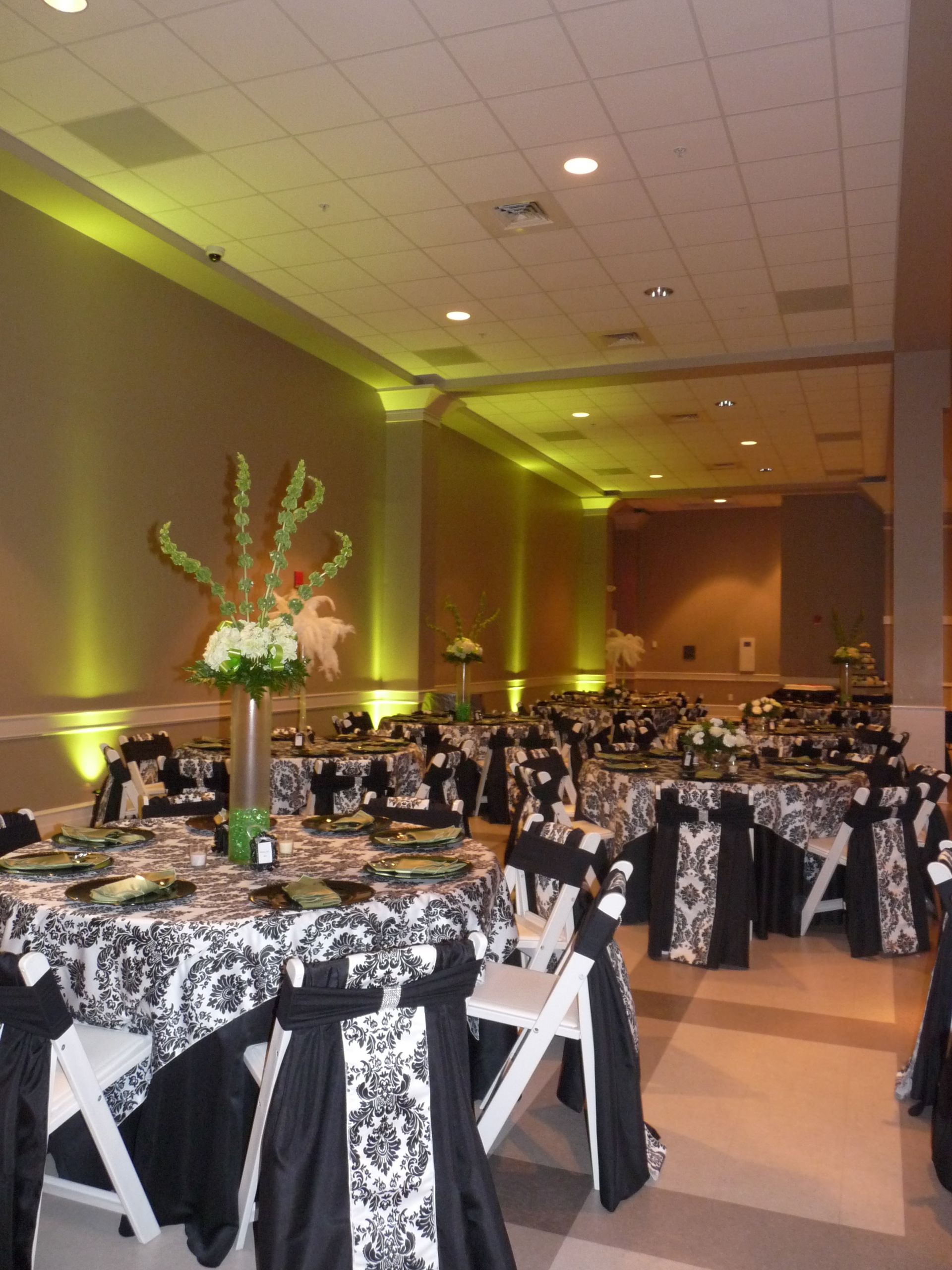 Banquet hall with black-and-white decorated tables and green uplighting along the walls