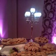 Dessert table with pastries and a lit candelabra against purple uplighting
