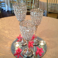 Three crystal goblets on a mirrored tray with pink flowers around them