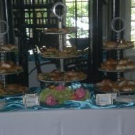 Tiered dessert table with pastries, flowers, and white tablecloth in front of windows