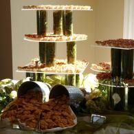 Tiered buffet display with stacked dishes of food and fruit on white shelves, lit indoors