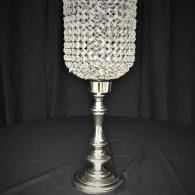 Tall silver candlestick with a crystal-covered top against a black draped background