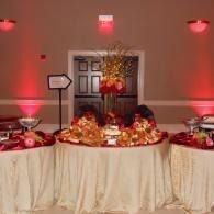 Red-lit buffet table with ornate gold centerpieces and desserts at an indoor event