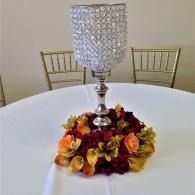 White table centerpiece with crystal candle holder and autumn-colored flowers on a round table.