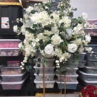 White floral arrangement in a store display with stacked plastic bins in the background