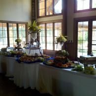 Buffet table with assorted food and floral arrangements by large sunlit windows