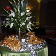 Floral centerpiece on a banquet table with plates of hors d'oeuvres and a green tablecloth