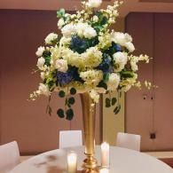 Tall gold floral centerpiece with white and blue flowers on a banquet table