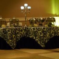 Elegant buffet table with floral tablecloth, silver serving dishes, and a candelabra in warm lighting