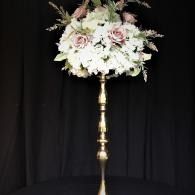 White and pale pink floral arrangement on a tall gold stand against a black backdrop