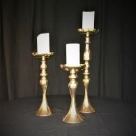 Three gold candlesticks with white candles on a black backdrop