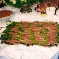 Large platter of sliced meat garnished with green herbs at a buffet table