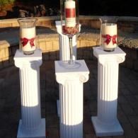 Three white pedestals with glass candle holders and red heart decorations outdoors at dusk